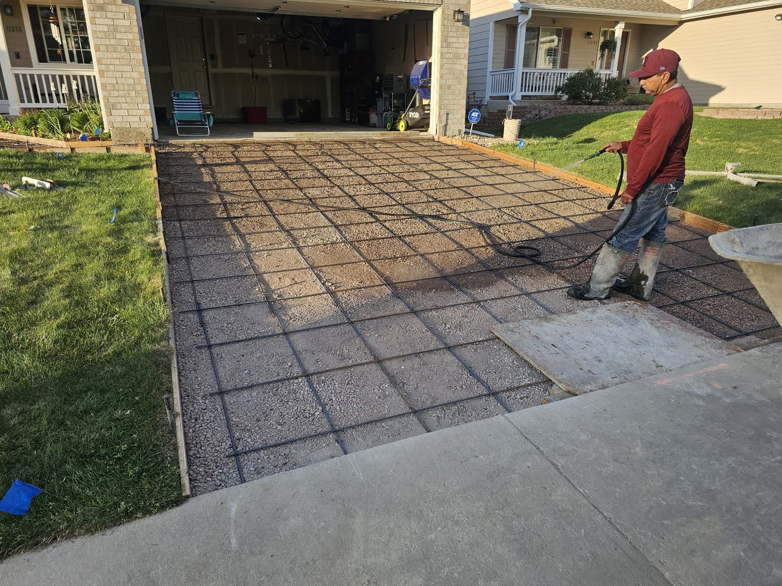 A crew member wetting a compacted gravel base inside wooden forms