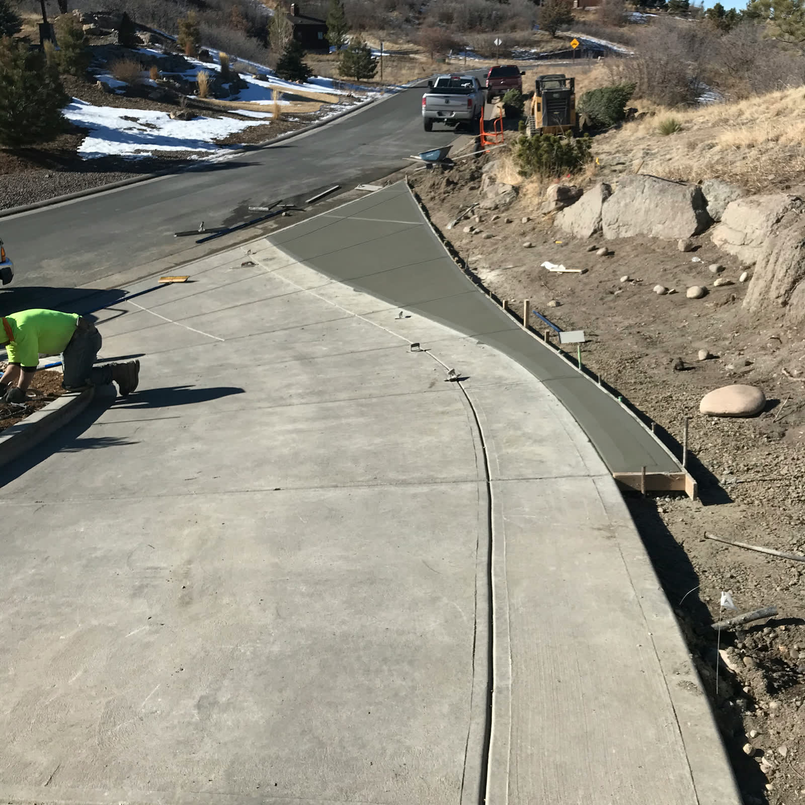 A finisher kneeling beside a freshly poured curved sidewalk