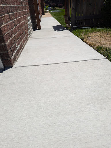 A narrow sidewalk poured tight along a brick wall, matched to the old height