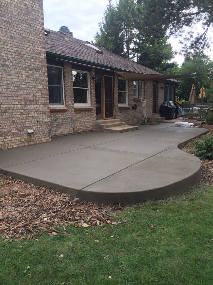 A large backyard patio with a long curved edge beside a brick house